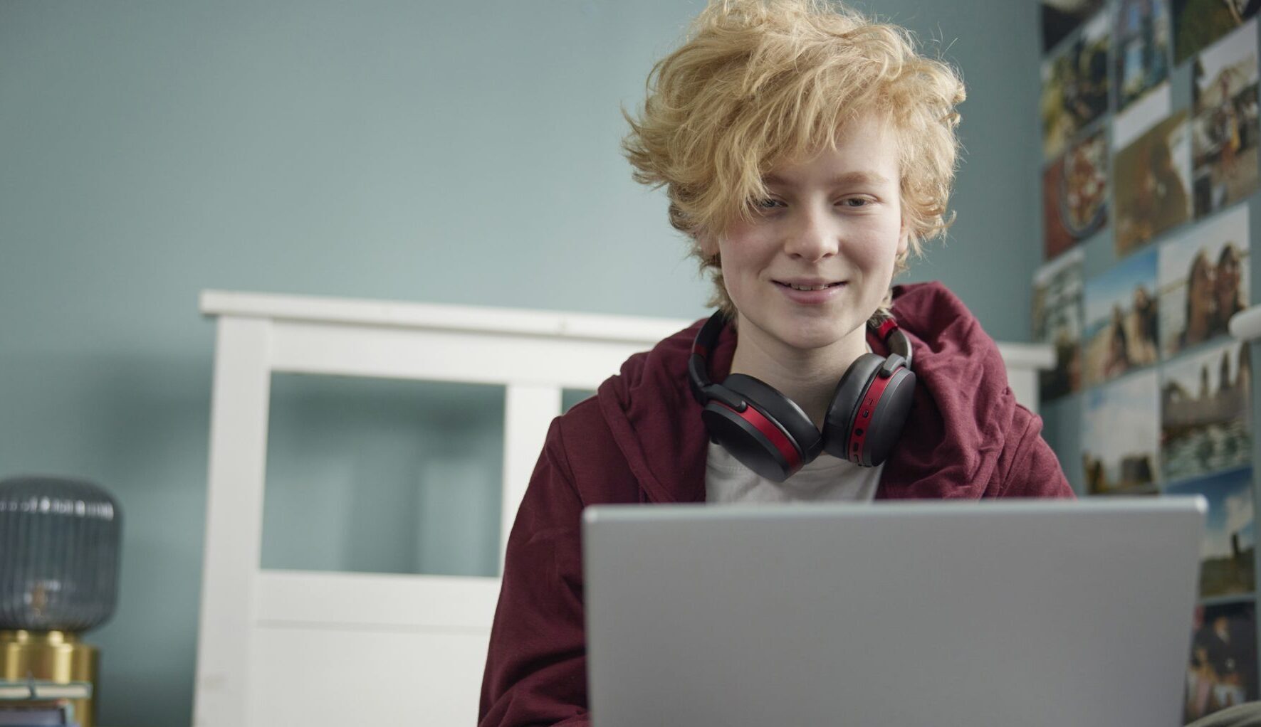 a teenage boy is wearing black headphones and is smiling straight at his laptop screen