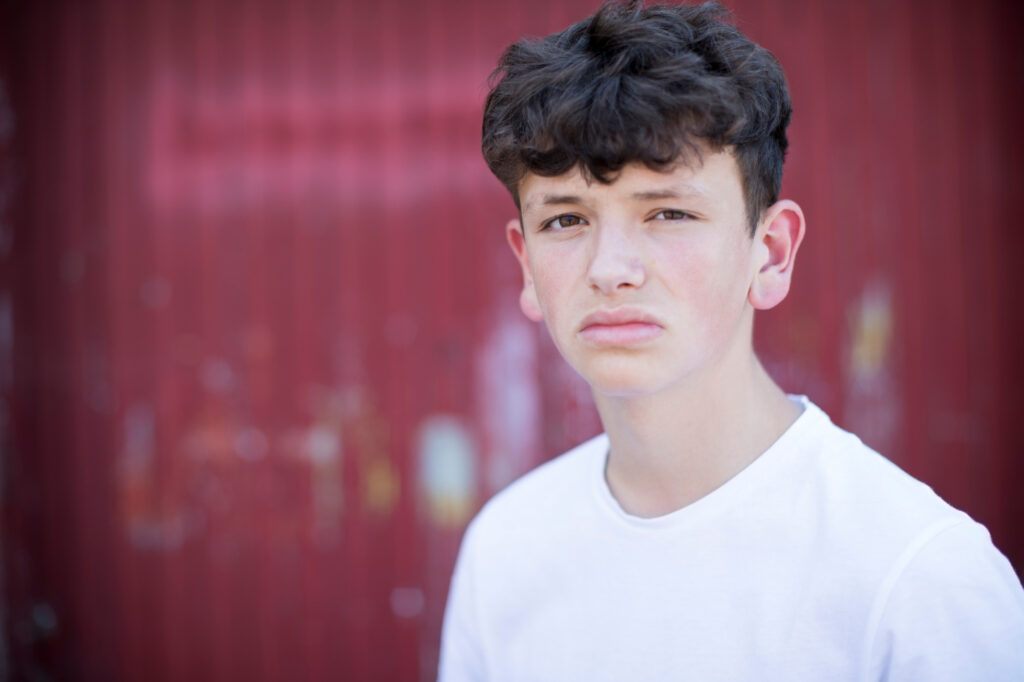 a teenage boy with short dark hair and dark eyes is looking straight at the camera with a serious expression