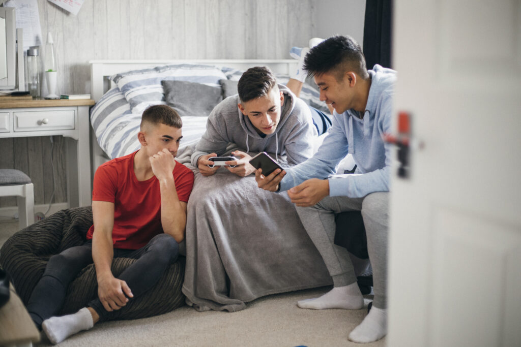 three teenage boys are sitting around a bed and looking at one of their mobile phones
