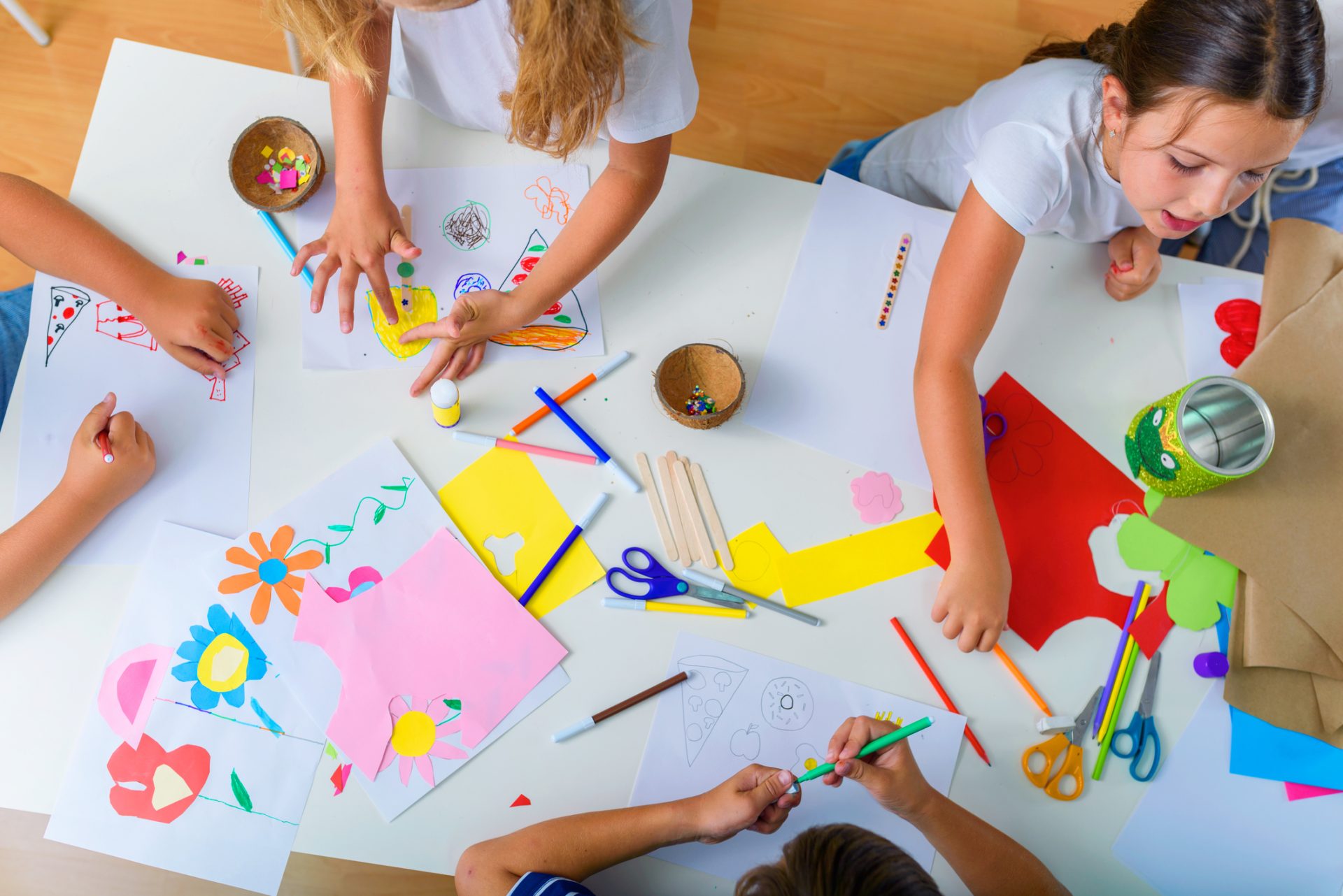 the arms of four children can be seen from above who are using art materials to draw pictures