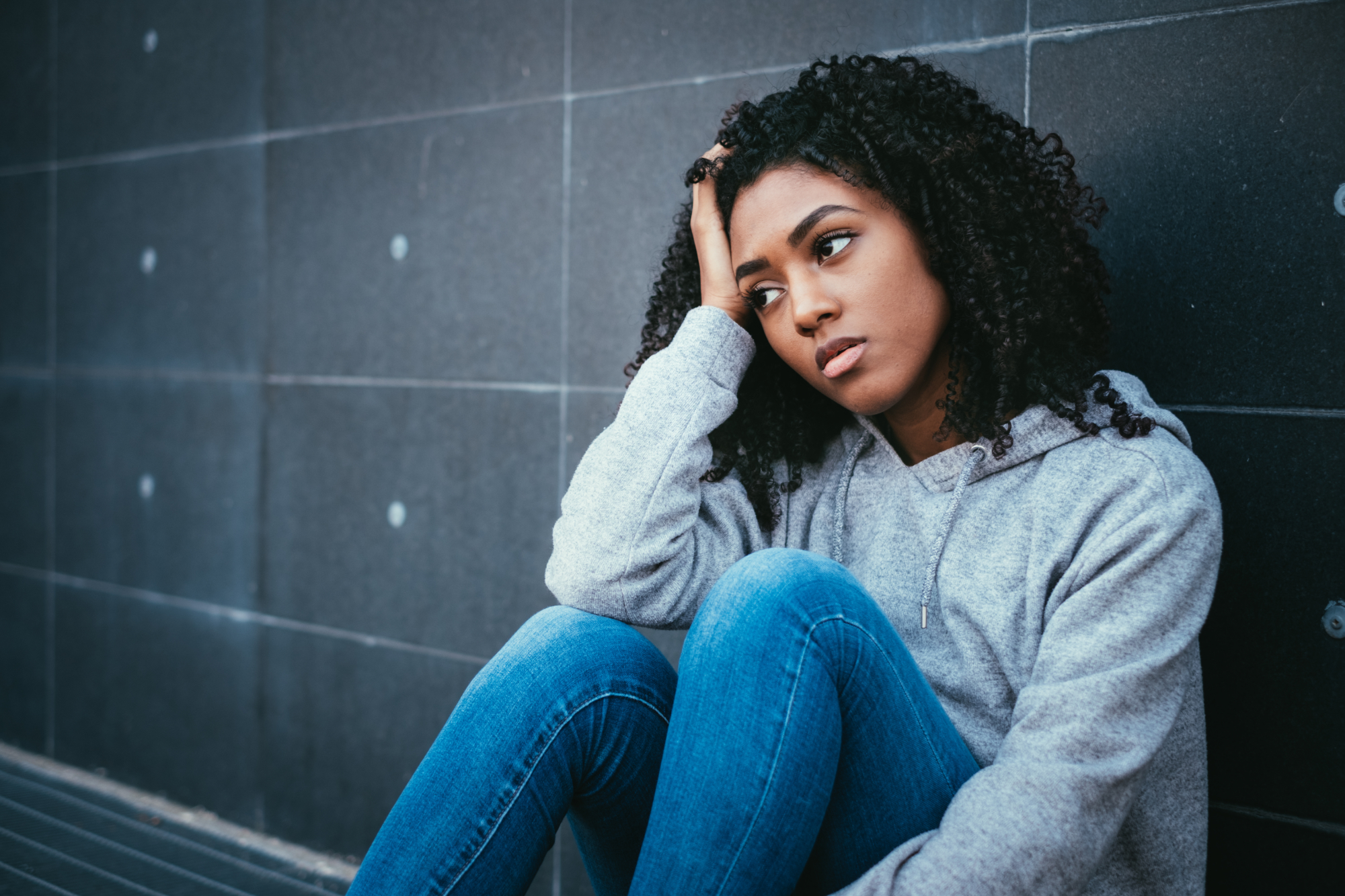 a teenage girl is sitting down against a wall with her head resting on her right hand