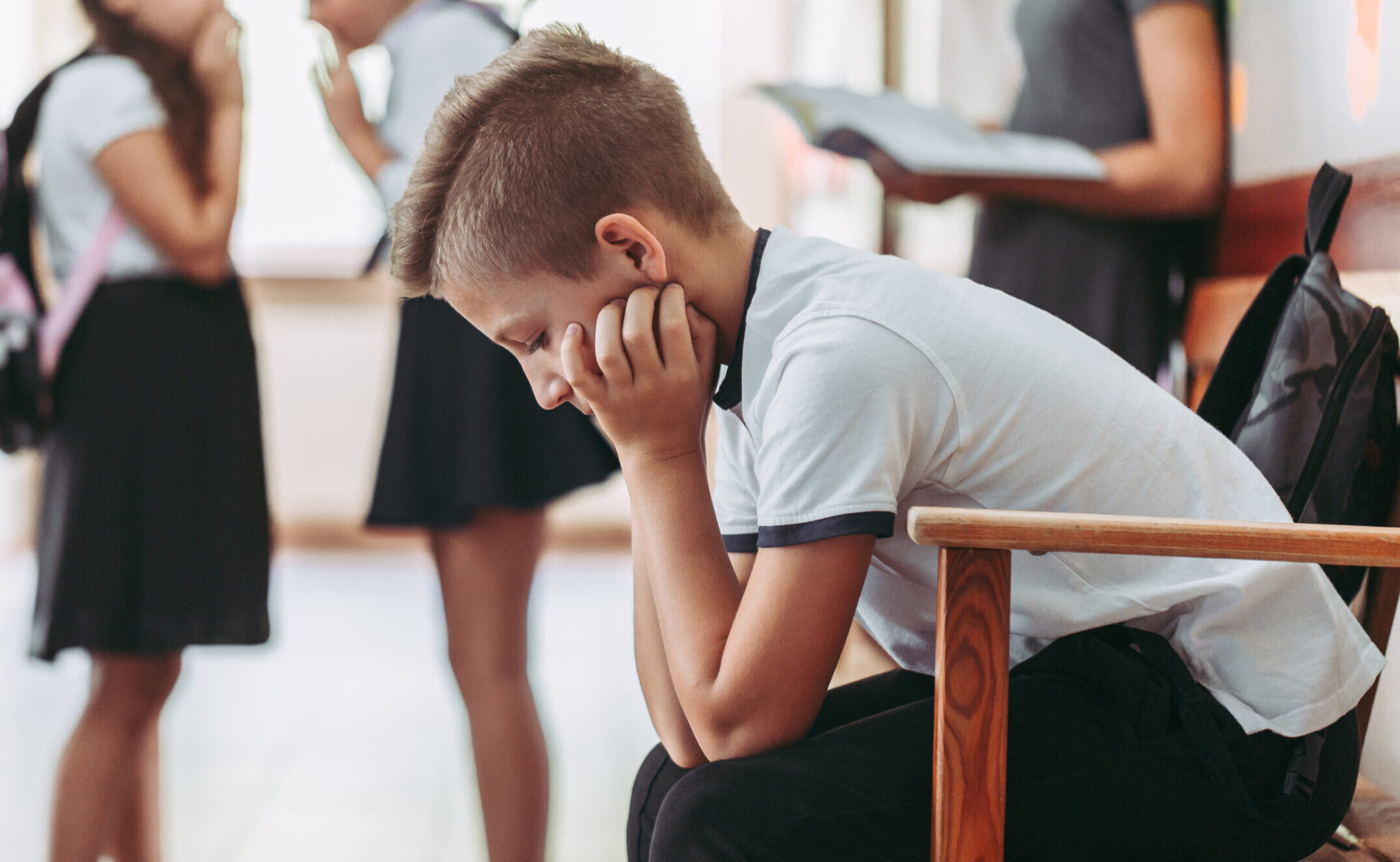 a young boy is sitting in a chair with his arms on his lap and hands on his face looking down at the floor with a sad expression