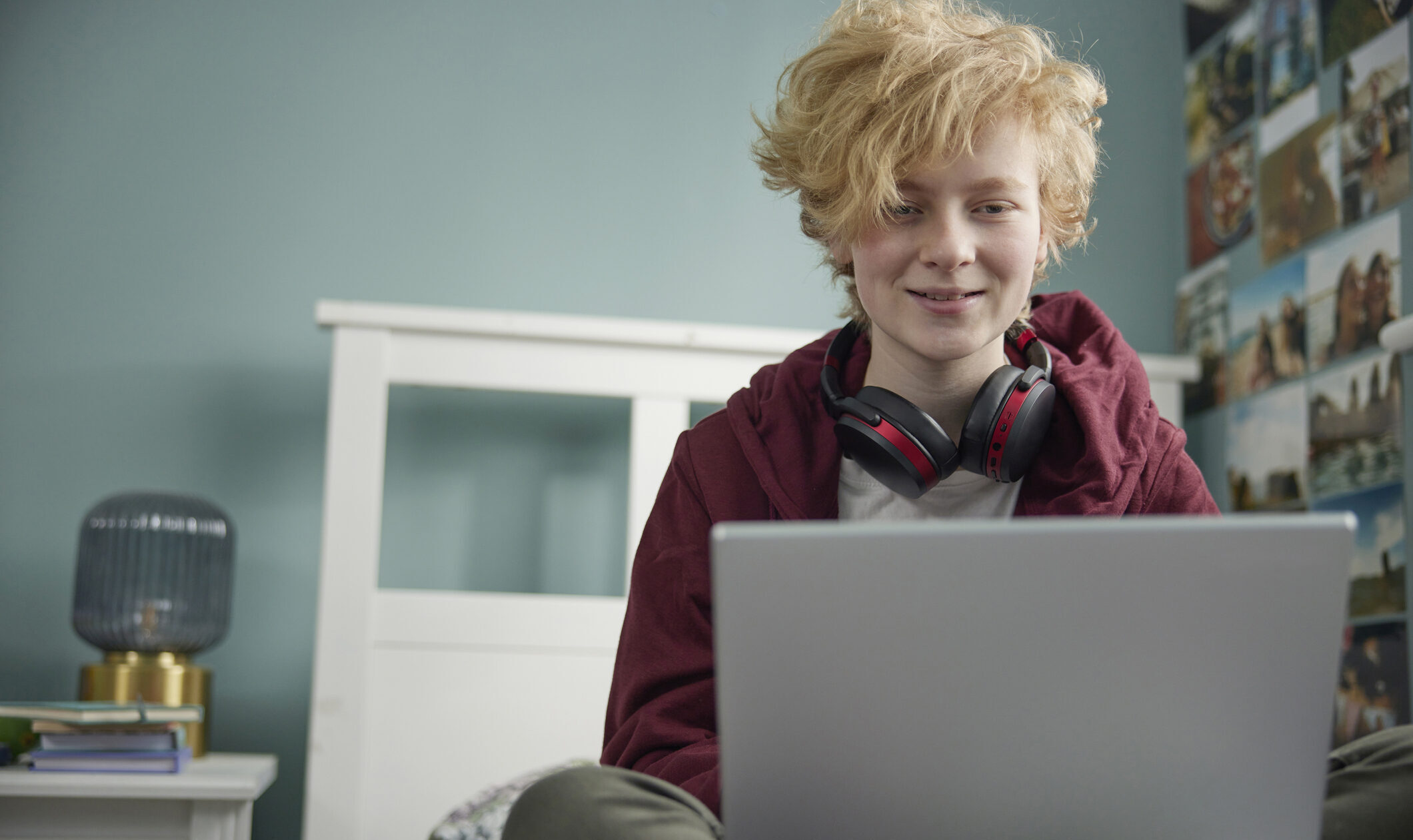 a teenage girl is wearing black headphones and is smiling straight at his laptop screen