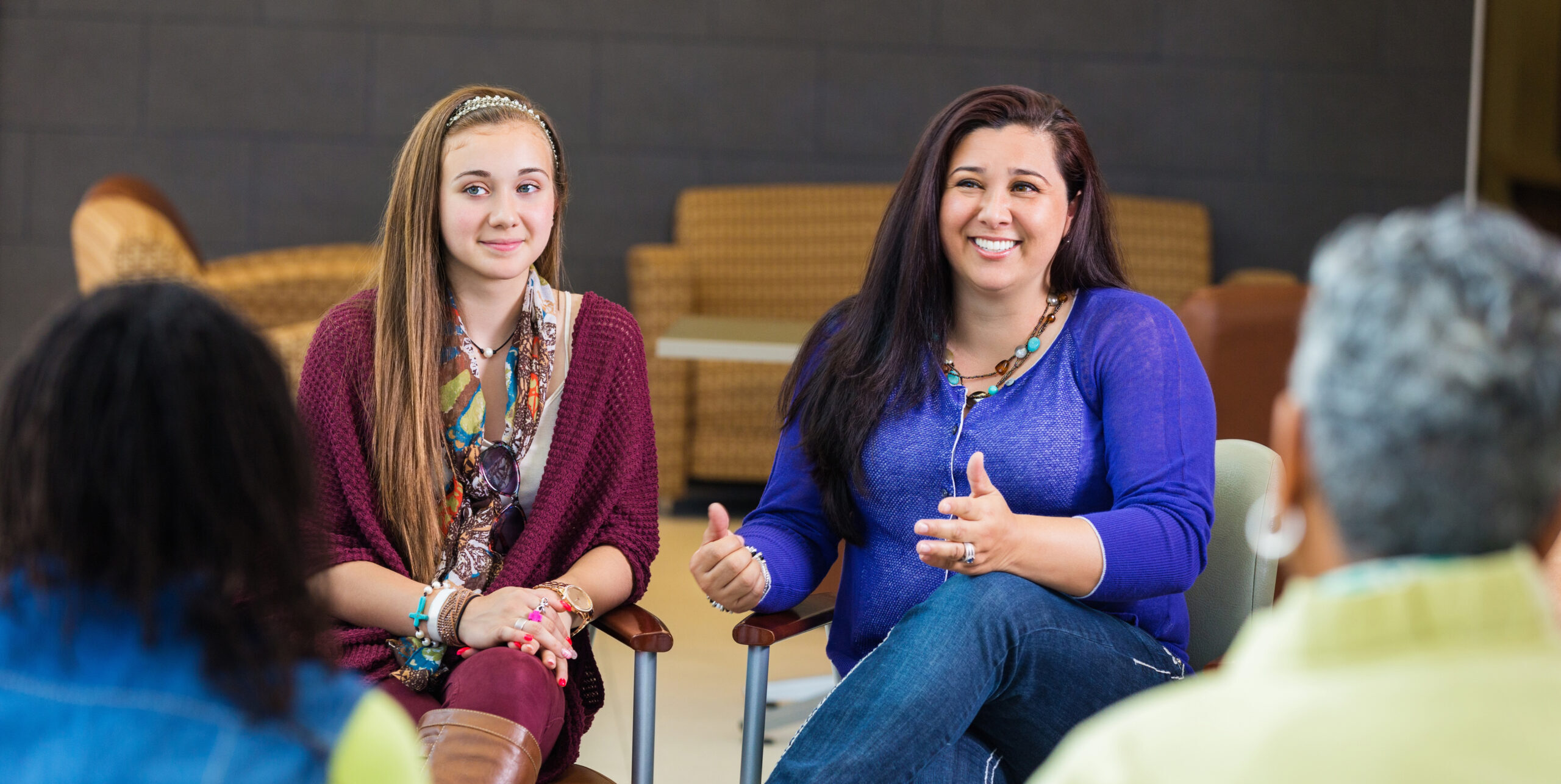 the photo shows a young girl sitting next to a female adult who is smiling at looking at someone opposite her in the group circle meeting