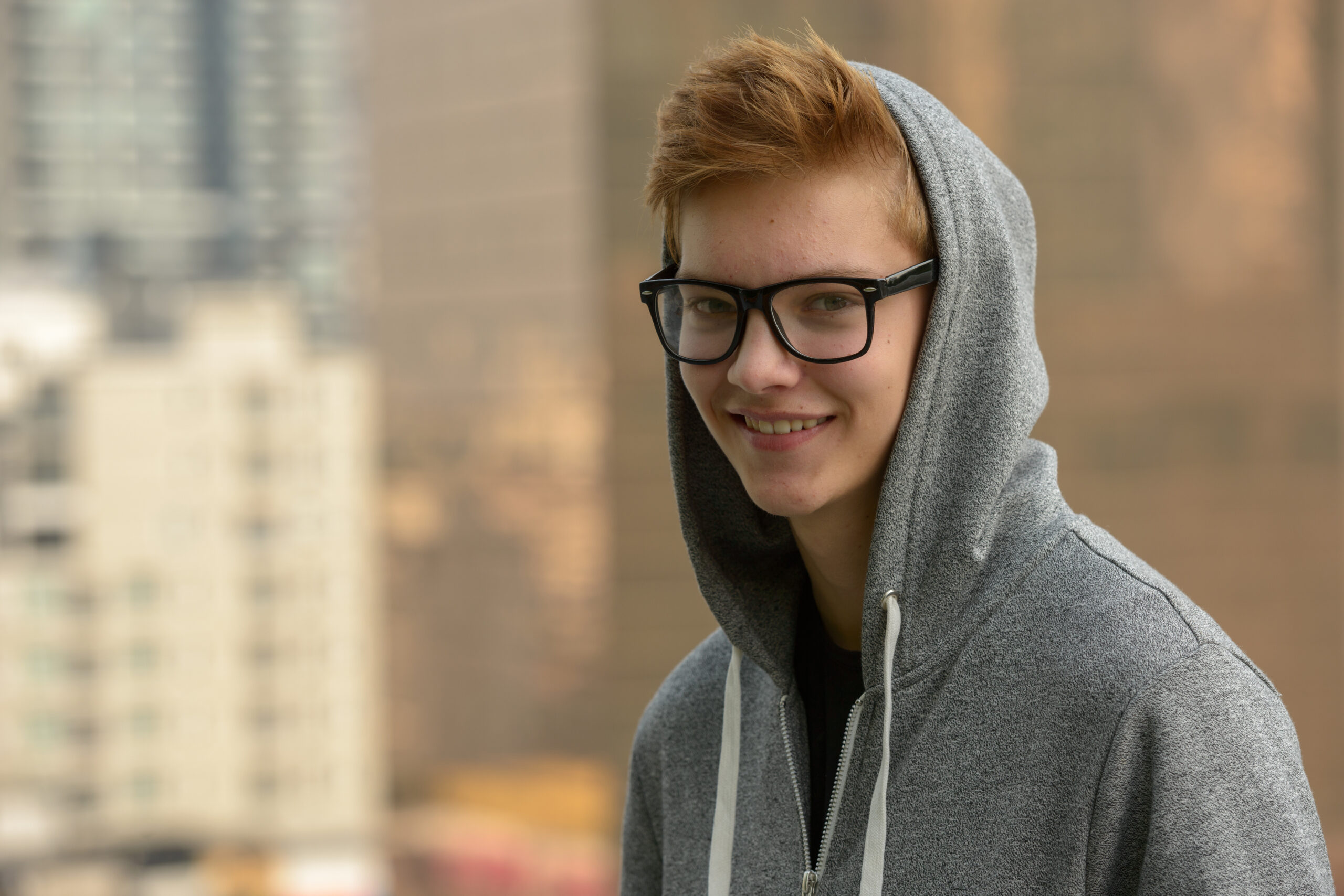a teenage boy is wearing a grey hoodie and glasses and is smiling straight at the camera