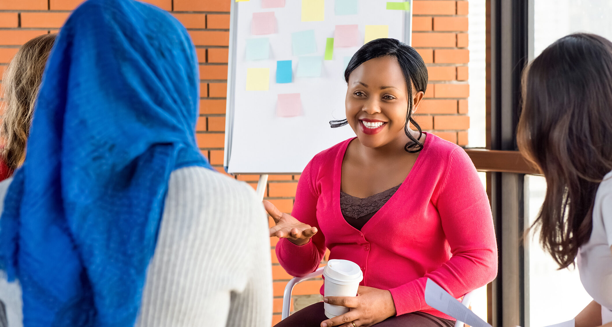 The photo shows a diverse group of women in colourful clothes at the meeting, discussing something and smiling