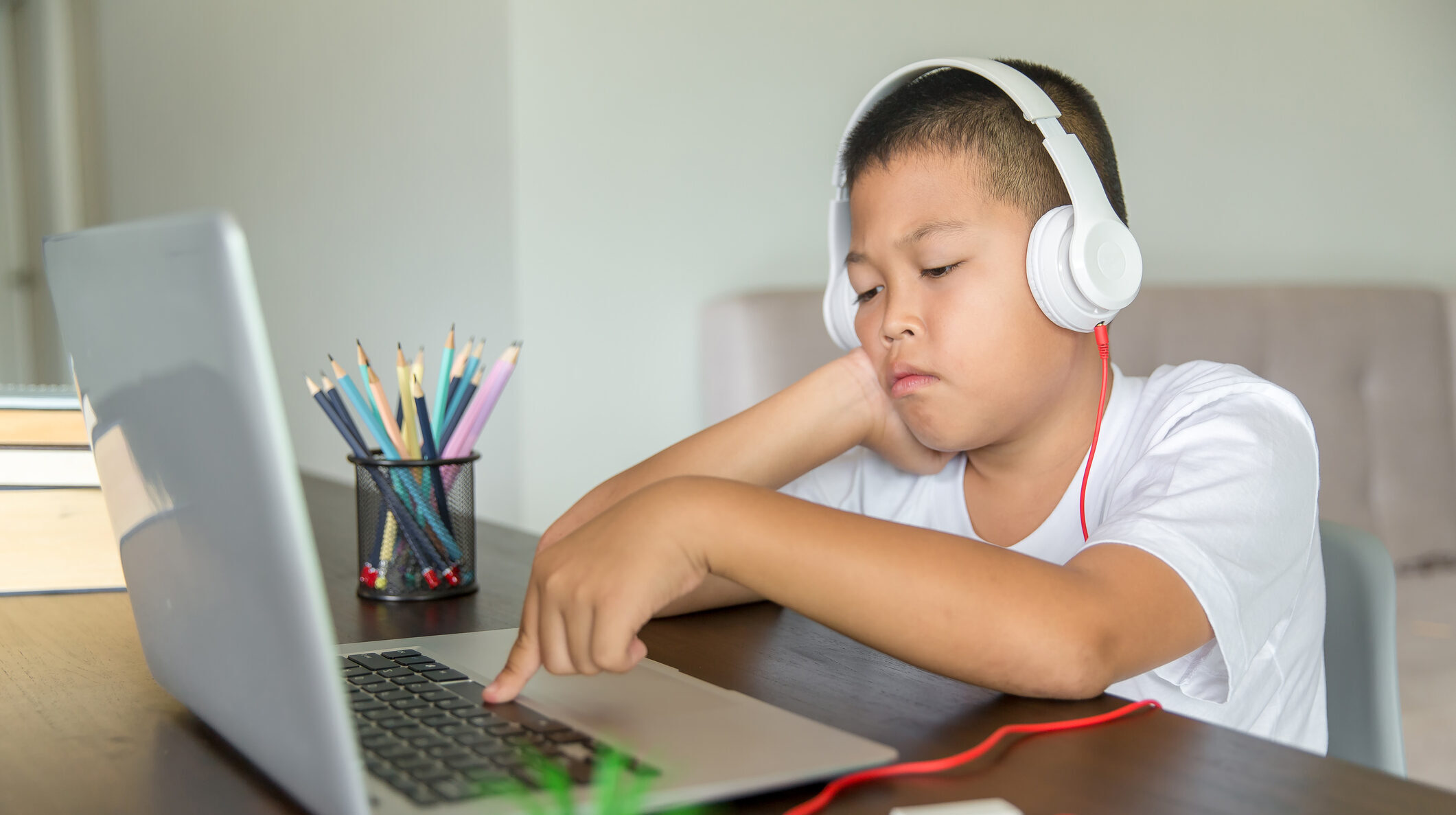 the photo shows a boy with short dark hair who is wearing white headphones and pressing the space bar on a laptop computer