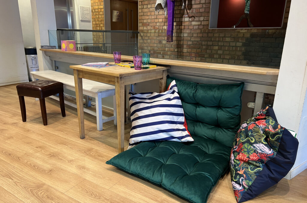 the photo shows a sitting area that contains big cushions and two small tables that contain plastic glasses and colouring books and pens